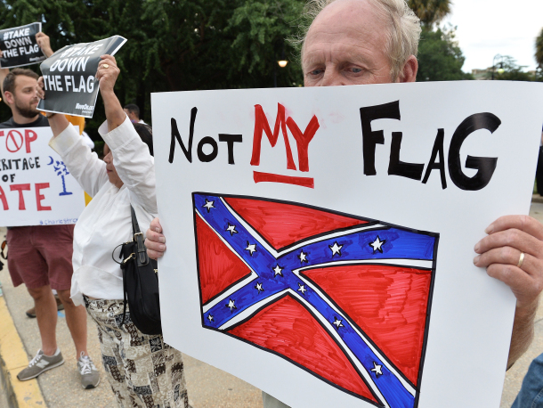 A man holds a sign up during a protest rally against the Confederate flag in Columbia, South Carolina on June 20, 2015. The racially divisive Confederate battle flag flew at full-mast despite others flying at half-staff in South Carolina after the killing of nine black people in an historic African-American church in Charleston on June 17. Dylann Roof, the 21-year-old white male suspected of carrying out the Emanuel African Episcopal Methodist Church bloodbath, was one of many southern Americans who identified with the 13-star saltire in red, white and blue. AFP PHOTO/MLADEN ANTONOV        (Photo credit should read MLADEN ANTONOV/AFP/Getty Images)
