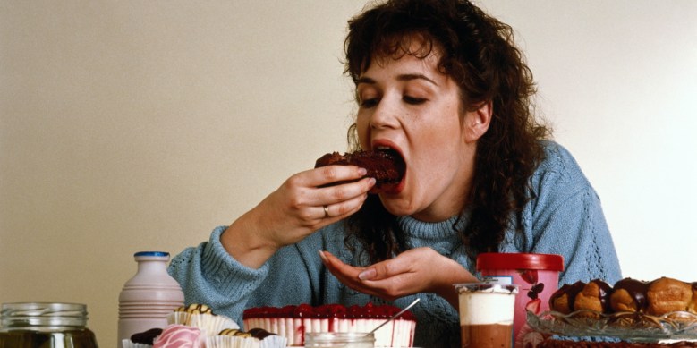 Woman sitting at food covered table eating piece of chocolate cake